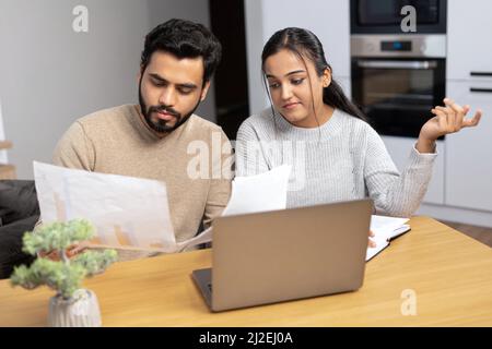 Serious young couple study documents together, have serious looks, dressed in casual wear, plan their budget, pose in spacious light room, do paperwork, busy preparing financial report Stock Photo