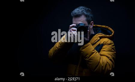 Photographer in a yellow coat taking a photo with a black background Stock Photo