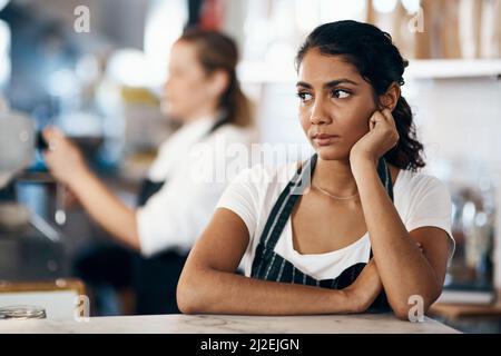 Could a change in career be on the menu. Shot of a young woman looking unhappy while working behind the counter of a cafe. Stock Photo