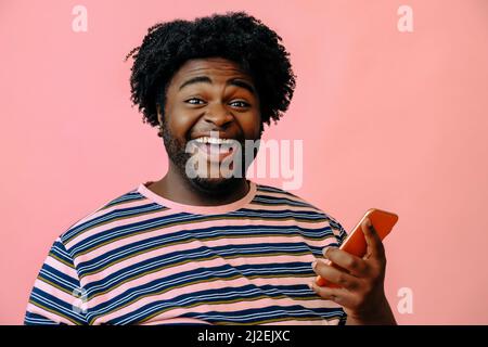 young happy black man with smart phone in the studio over pink background male model Stock Photo
