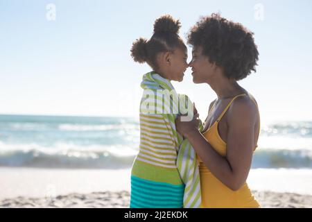 Side view of african american mother and daughter rubbing noses at beach on sunny day Stock Photo