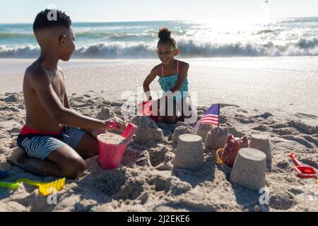 Happy african american siblings making sandcastle together at beach on sunny day Stock Photo