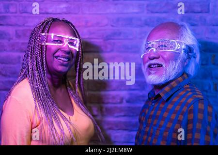 Happy senior friends having fun with futuristic augmented reality glasses - Metaverse concept Stock Photo