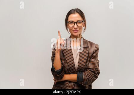 Happy woman in formal suit pointing finger up with smile, paying attention to empty space for your advertisement, template. Indoor studio shot isolated on white background Stock Photo