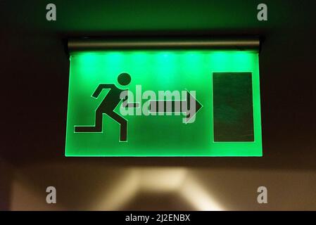 Green fire escape sign hang on the ceiling in the office. Stock Photo