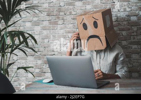 People at work with sad carton box on head diong phone call in front of a laptop on the desk. Sad worker anonymous. Business fail activity and unhappy Stock Photo