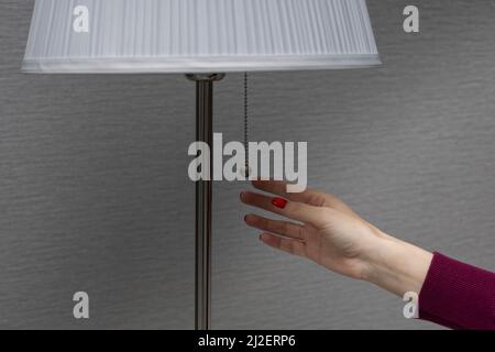 a woman turns on a floor lamp by pulling the switch chain. High quality photo Stock Photo