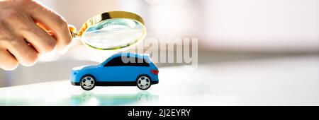 Person Scrutinizing A Car Model Using Magnifying Glass On Desk Stock Photo