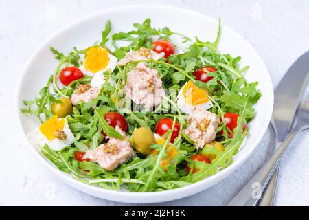 Salad with tuna, arugula, tomatoes, olives and eggs in a white plate. A traditional dish. Close-up. Stock Photo