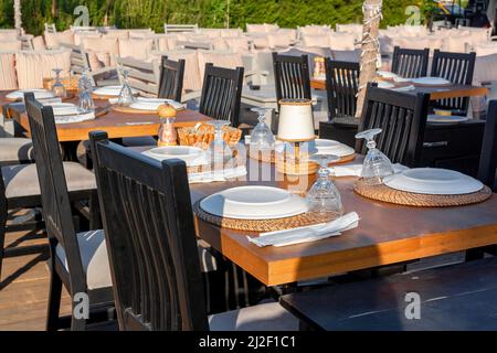 Many wooden tables in cafe with plates and glasses are waiting for guests. Horizontal photo. Stock Photo