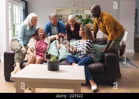 Happy multiracial senior male and female friends looking at digital tablet at home Stock Photo