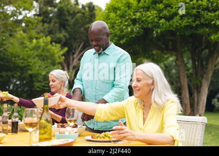 Multiracial senior male and female friends enjoying wine at table during backyard party Stock Photo