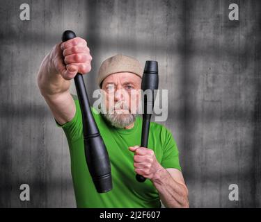 senior man (in late 60s) is exercising Indian clubs, portrait against dark grunge background, fitness over 60 concept Stock Photo