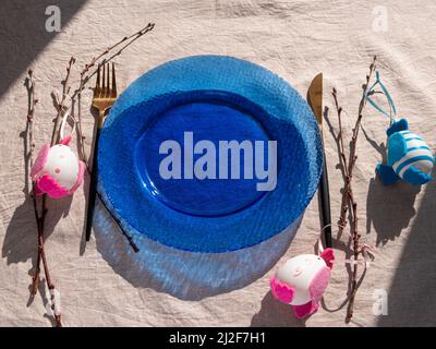 Easter table setting empty blue glass plate fork knife tree branches linen cloth top view harsh shadow. Festive dish place Natural cottagecore styled Stock Photo