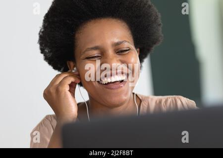 Cheerful mid adult african american female freelancer using earphones while working on laptop Stock Photo
