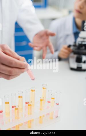 cropped view of geneticist holding test tube near blurred colleague and microscope,stock image Stock Photo