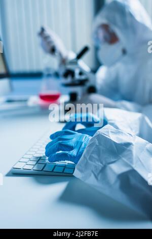 scientist in latex gloves typing on computer keyboard while colleague working on blurred background,stock image Stock Photo