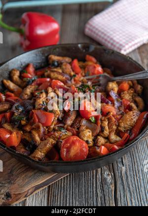 Pan dish with meat and vegetables in a rustic cast iron pan on wooden table. Stock Photo