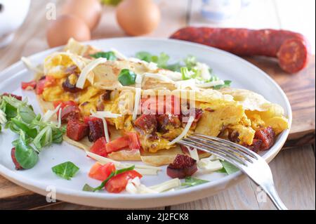 Crepe or pancake filled with scrambled eggs, tomatoes, cheese and fried chorizo salami. Served on a plate for a savory breakfast Stock Photo