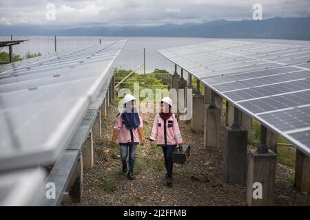 Female electrical technicians in uniform inspect and maintain solar panels on Karampuang Island, Indonesia, Asia. Stock Photo
