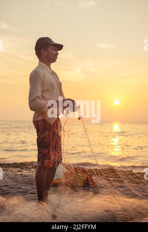 Kochi, India - Junuary 22, 2015: Indian fisherman catches fish by the traditional method of throwing net into the sea at sunset. Kerala region. Stock Photo