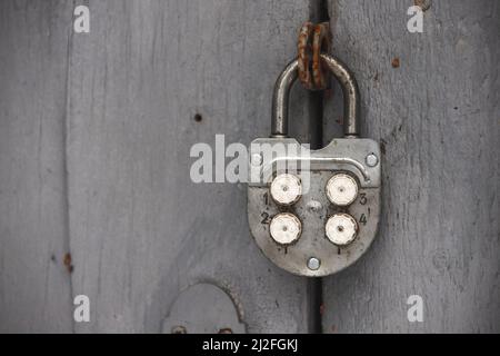 Old combination padlock hanging on grungy gray wooden door. Close up photo Stock Photo