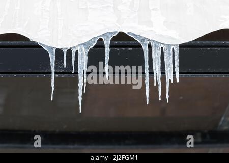 Icicles hang on living house roof, close up photo with selective focus Stock Photo