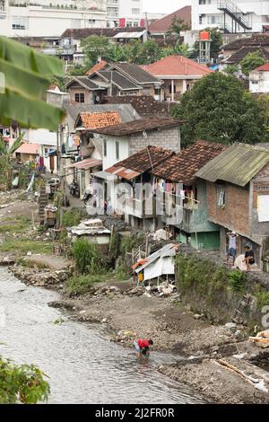 Crowded colorful slum dwellings sit along side a sewage drainage canal ...