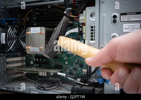 a hammer is held in front of an unscrewed PC Stock Photo