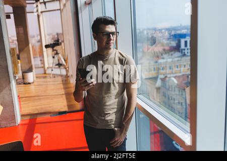 Cheerful scofe male entrepreneur standing near office window and smiling during working day in company, successful corporate boss feeling good from ri Stock Photo