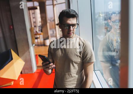 Cheerful scofe male entrepreneur standing near office window and smiling during working day in company, successful corporate boss feeling good from ri Stock Photo