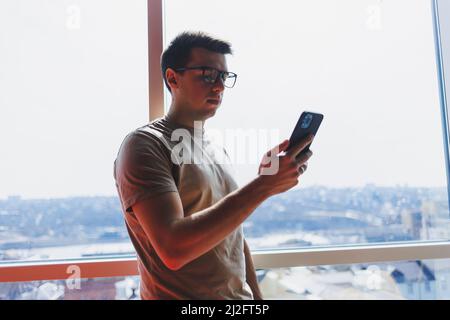 Cheerful scofe male entrepreneur standing near office window and smiling during working day in company, successful corporate boss feeling good from ri Stock Photo