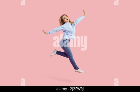 Happy cheerful dancer girl in sweatshirt and jeans jumping isolated on pink background Stock Photo