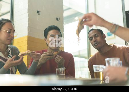 Smiling friends eating pizza at modern pizzeria restaurant - Friendship concept with multi ethnic people enjoying time together having fun at pizzeria Stock Photo