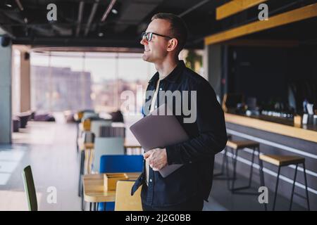 Male entrepreneur in black shirt and glasses standing in office with laptop in hand, successful corporate boss feeling good from rich lifestyle Stock Photo