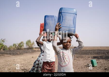 Three West African Pretty Girls,returning to the village, carrying plastic water containers on their heads.Water Supply in Rural Communities. Stock Photo