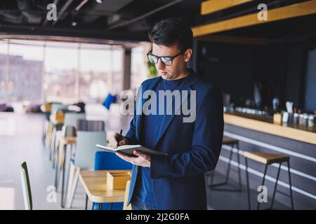 Young freelancer man working in a cafe with a notepad, a businessman with a notepad, a man in a jacket and glasses Stock Photo