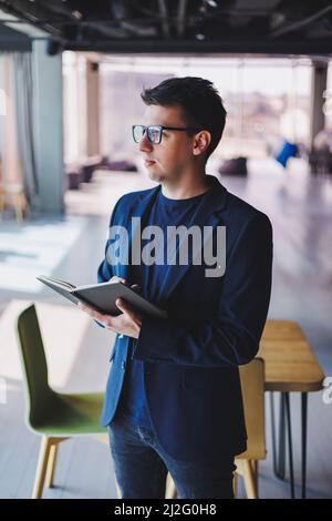 Young freelancer man working in a cafe with a notepad, a businessman with a notepad, a man in a jacket and glasses Stock Photo