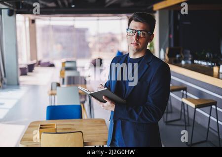 Young freelancer man working in a cafe with a notepad, a businessman with a notepad, a man in a jacket and glasses Stock Photo