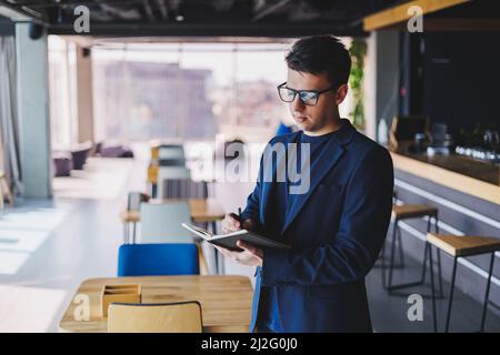 Young freelancer man working in a cafe with a notepad, a businessman with a notepad, a man in a jacket and glasses Stock Photo