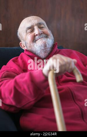 elderly man sitting with walking stick in his hand Stock Photo