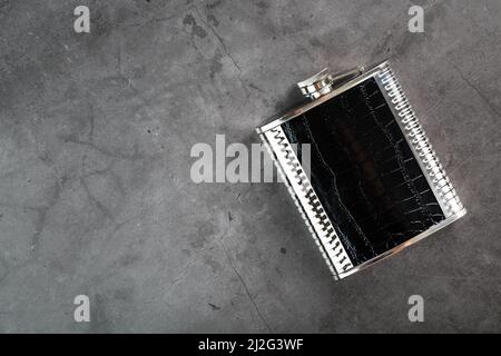 Pocket flask made of steel in leather finish with an alcoholic drink on a dark background with copy space Stock Photo