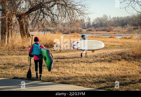 Evans, CO, USA - March 26, 2022: Female paddlers are carrying their inflatable stand up paddleboards to launch for early spring paddling trip on the S Stock Photo