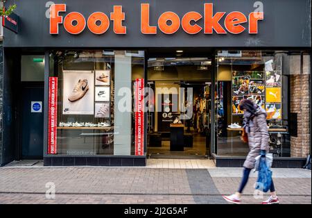 Kingston Upon Thames London UK, April 01 2022, Foot Locker High Street Retail Chain Shop Front With Woman Walking Past Carrying Shopping Bag Stock Photo