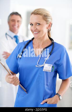 Youre in capable hands. Portrait of a female doctor in scrubs with a colleague standing in a the background. Stock Photo