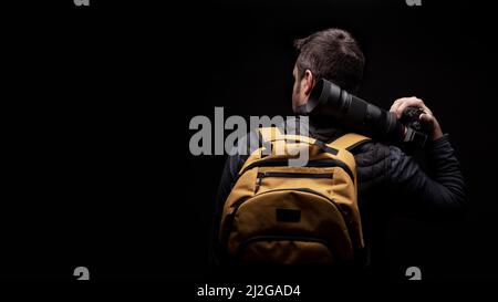 Photographer with a yellow bag is wearing a photo camera in a black background Stock Photo