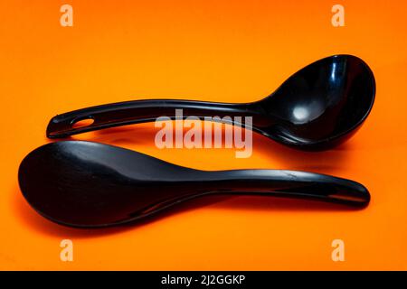 Set of kitchen spoon and spatula in black plastic isolated on orange background. Stock Photo