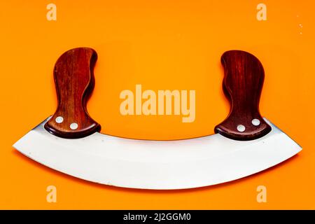 Mezzaluna knife with stainless steel blade and wooden handles insulated on orange background. Cutting kitchen utensils Stock Photo