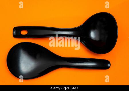 Set of kitchen spoon and spatula in black plastic isolated on orange background. Stock Photo