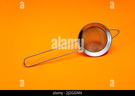 Hand strainer with fine metal mesh insulated on orange bottom. Stock Photo